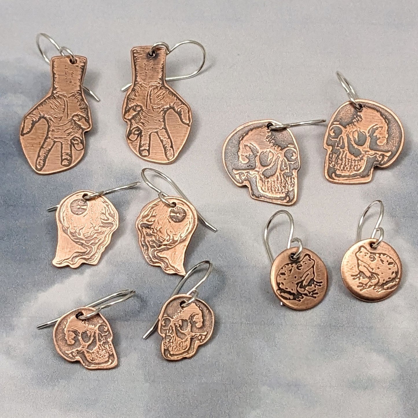 Copper earrings with halloween designs. hands, skulls, brains, and frogs