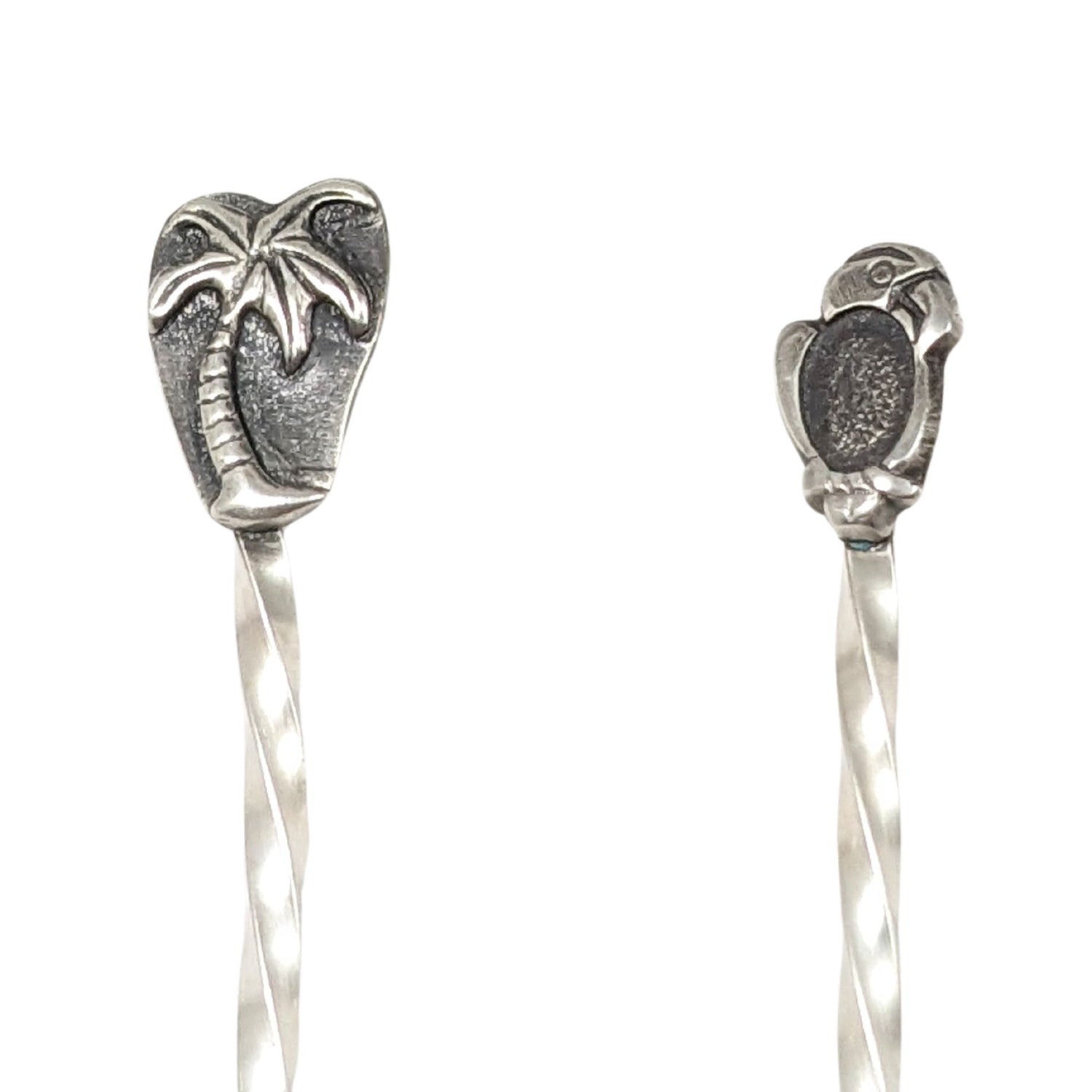 Pair of sterling silver cocktail picks. One has a palm tree, the other a parrot.
