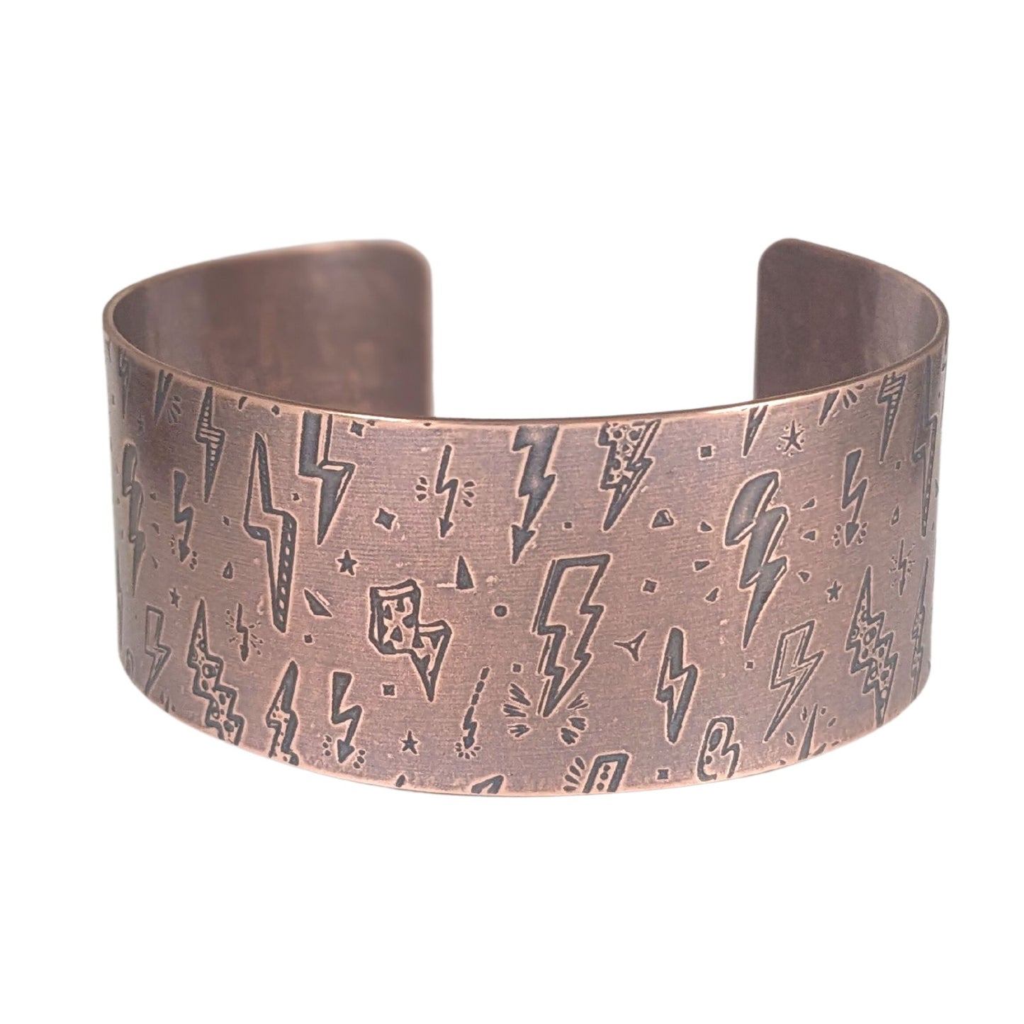 One inch wide copper cuff bracelet with an impressed pattern of assorted cartoon style lightning bolts. The bolts are darkened to accentuate the details.