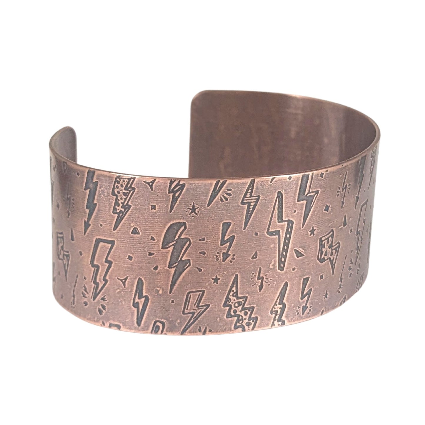 One inch wide copper cuff bracelet with an impressed pattern of assorted cartoon style lightning bolts. The bolts are darkened to accentuate the details.