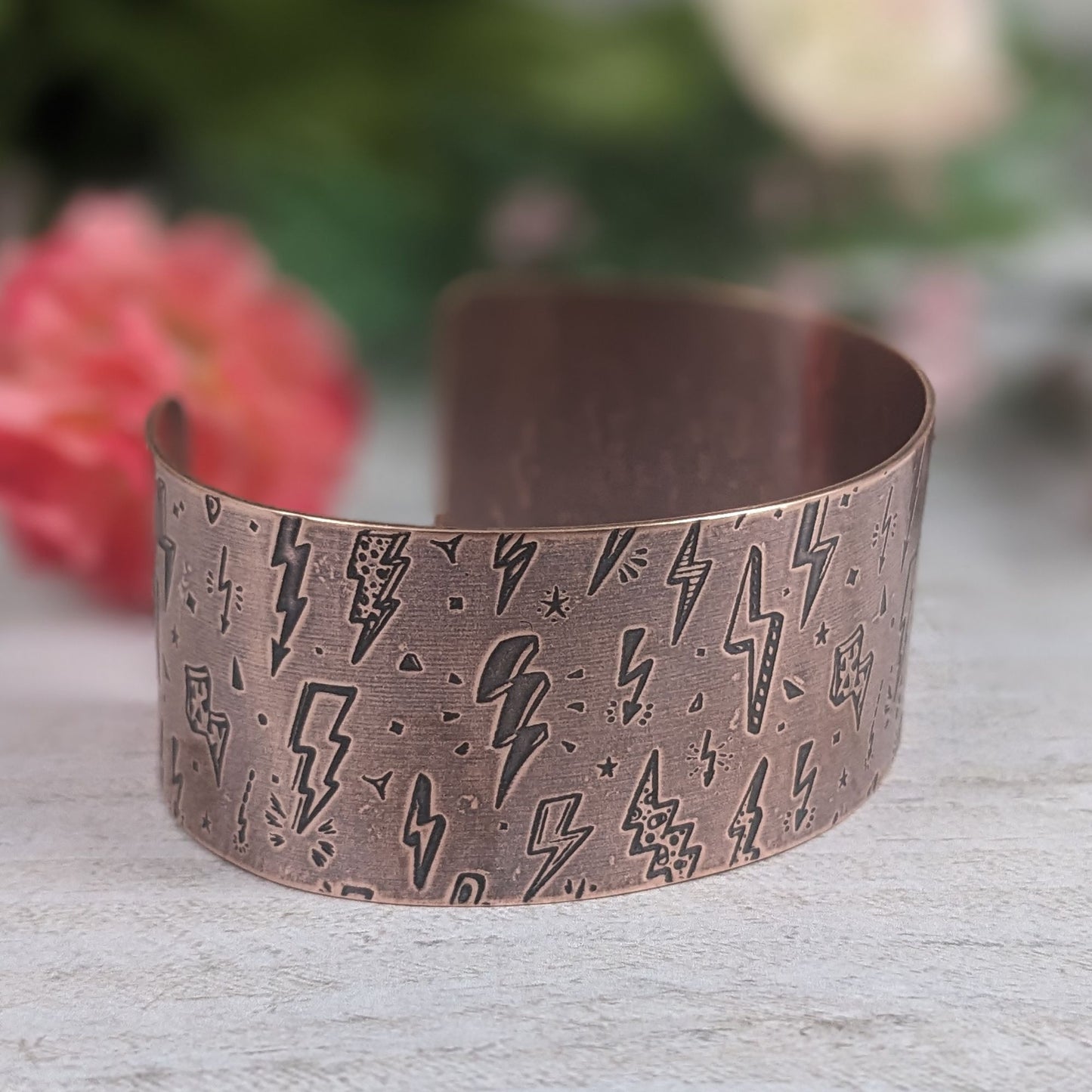 One inch wide copper cuff bracelet with an impressed pattern of assorted cartoon style lightning bolts. The bolts are darkened to accentuate the details.