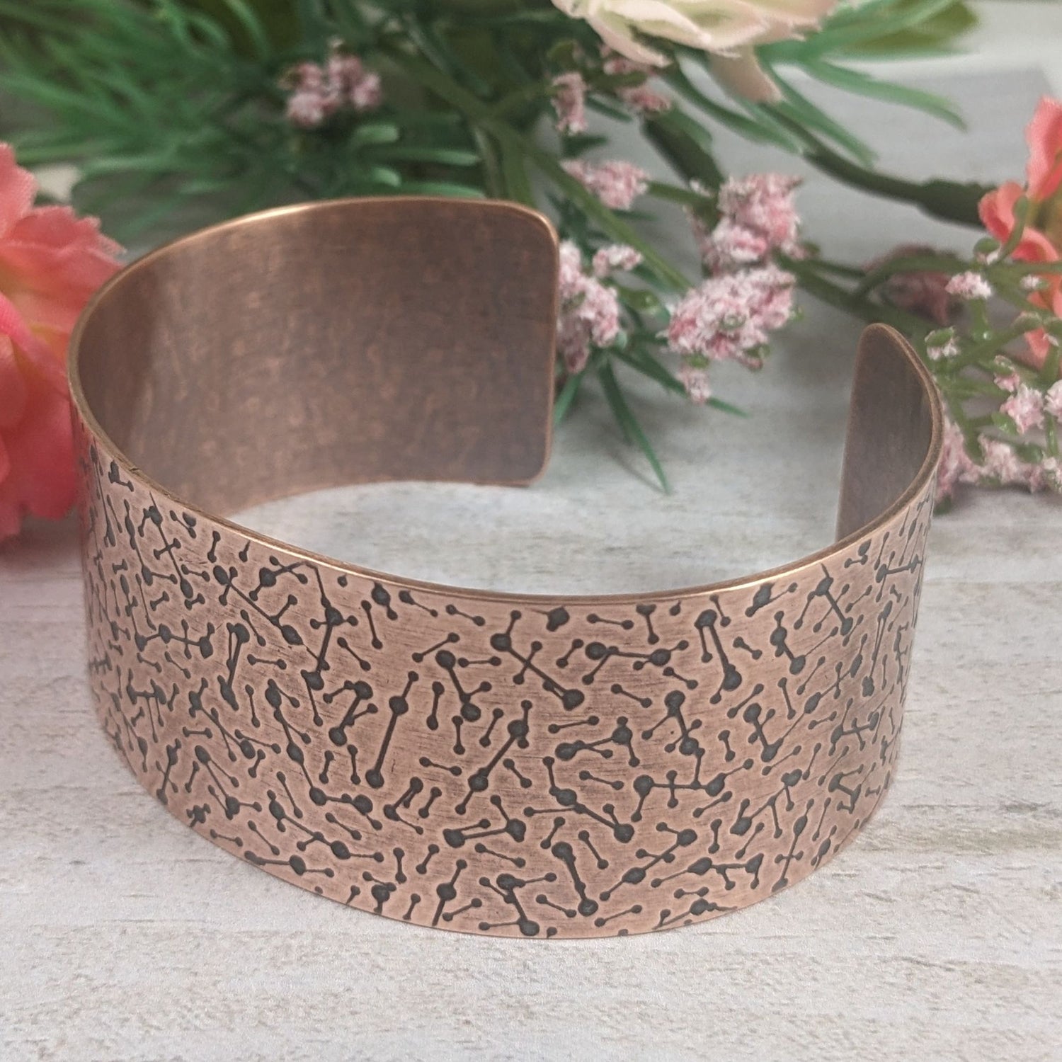 copper cuff covered in lines with dots on the ends to represent a meteor design