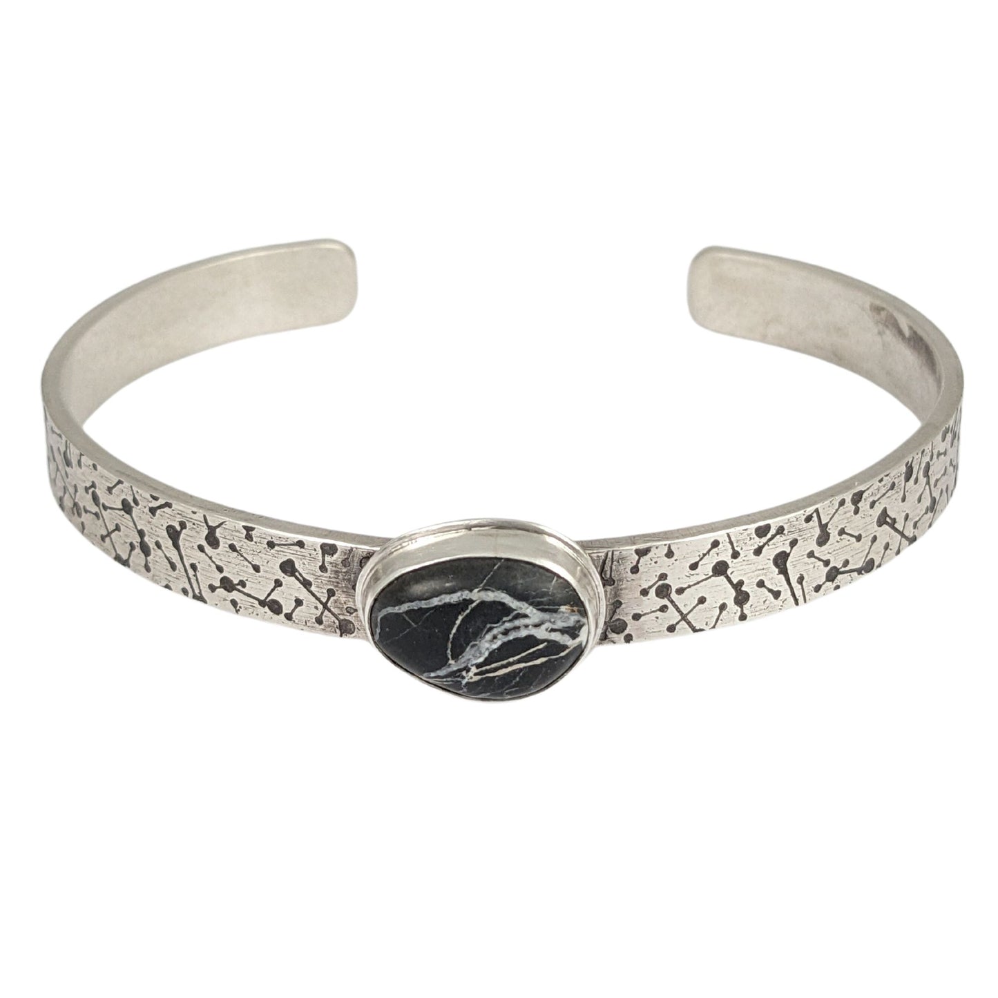 8 millimeter wide sterling silver cuff bracelet. The silver is covered in short lines with small dots on the ends that represent meteor showers. On the center is a freeform oval shaped white buffalo stone, which is a black stone with random streaks of white running through it.