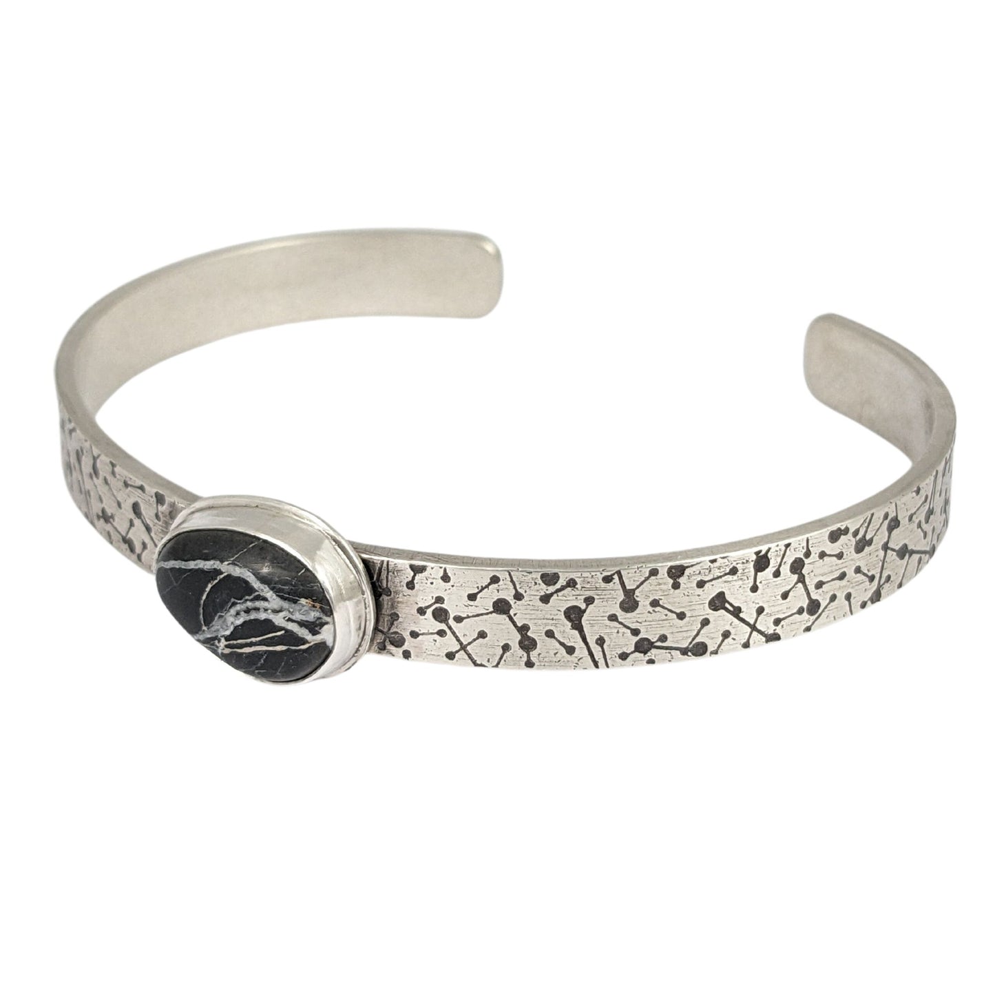 8 millimeter wide sterling silver cuff bracelet. The silver is covered in short lines with small dots on the ends that represent meteor showers. On the center is a freeform oval shaped white buffalo stone, which is a black stone with random streaks of white running through it.