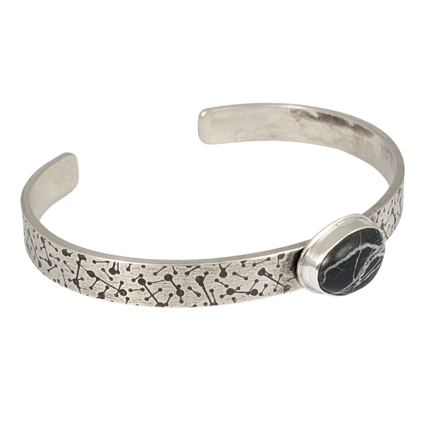 8 millimeter wide sterling silver cuff bracelet. The silver is covered in short lines with small dots on the ends that represent meteor showers. On the center is a freeform oval shaped white buffalo stone, which is a black stone with random streaks of white running through it.