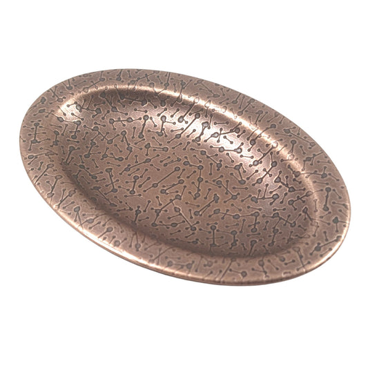 Oval ring dish made of copper. The dish has a shallow bowl with a lip around the edge. It is covered in a pattern meant to represent a meteor shower. The pattern is impressed into the copper and is short lines with small solid circles at the end. The design is oxidized, which means the impressed parts are dark, almost black.