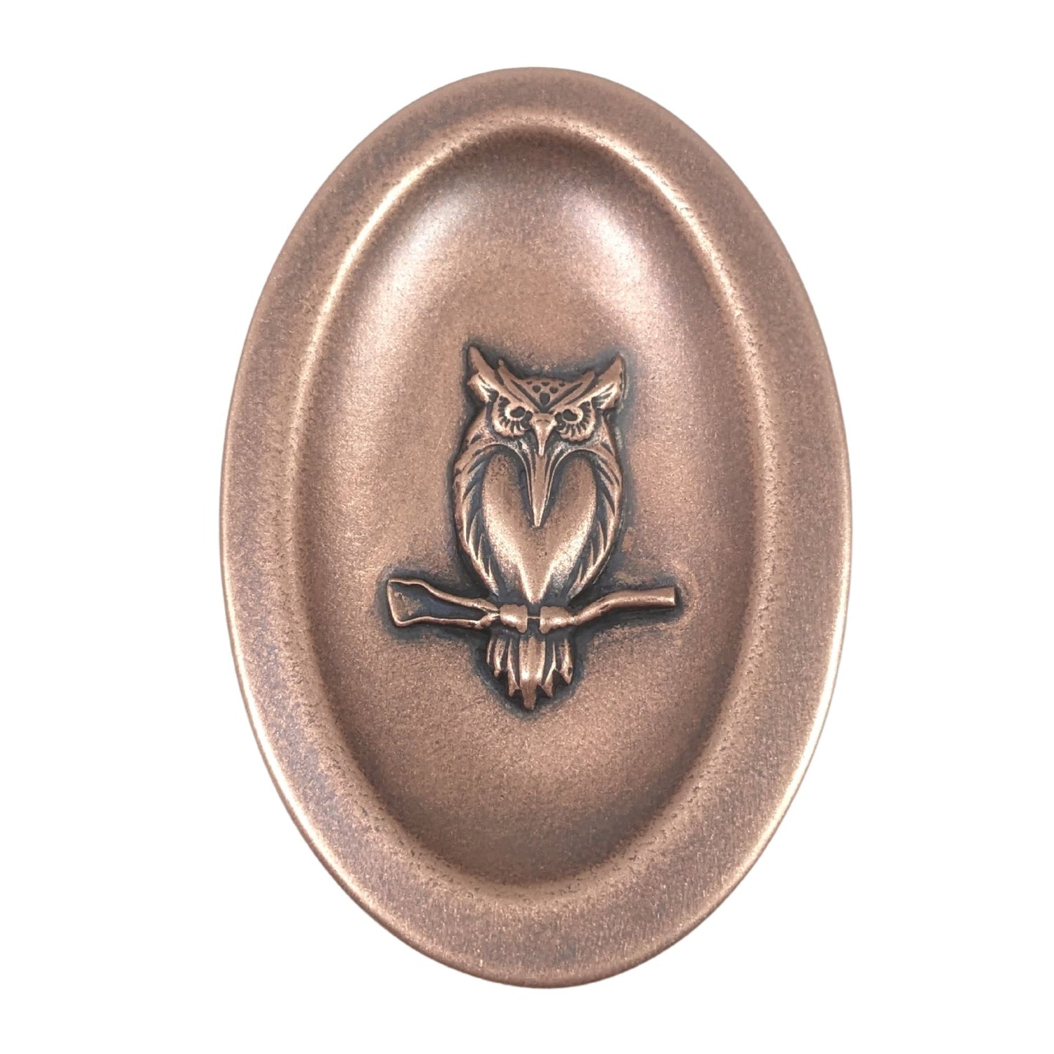 Oval ring dish made of copper. The dish has a shallow bowl with a lip around the edge. Centered on the bottom of the dish is a three-dimensional design of an owl, also made of copper. The owl is facing straight ahead and is perched on a branch. The breast is smooth and shaped like a long narrow heart. The owl hd large eyes, a pointed beak, tufted ears, and feathers around the breast and on the tail.  The design is oxidized, which means the recessed parts of the owl are dark, almost black.