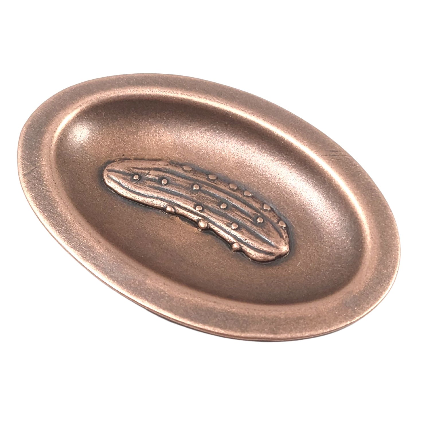 Oval ring dish made of copper. The dish has a shallow bowl with a lip around the edge. Centered on the bottom of the dish is a three-dimensional design of a pickle, also made of copper. The pickle is large and has stipples and ridges, just like a fresh from the garden pickle would have.  The design is oxidized, which means the recessed parts of the pickle are dark, almost black.