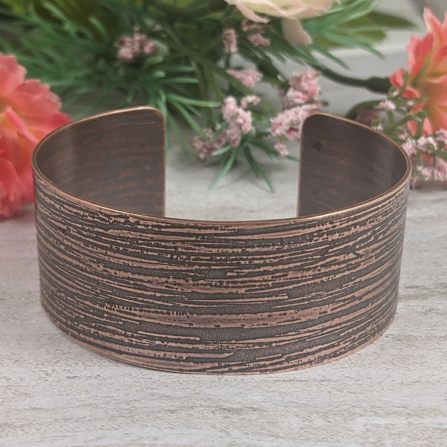 One inch wide copper cuff bracelet with an impressed texture that resembles raw silk fabric. The texture is horizontal and covers the entire cuff.