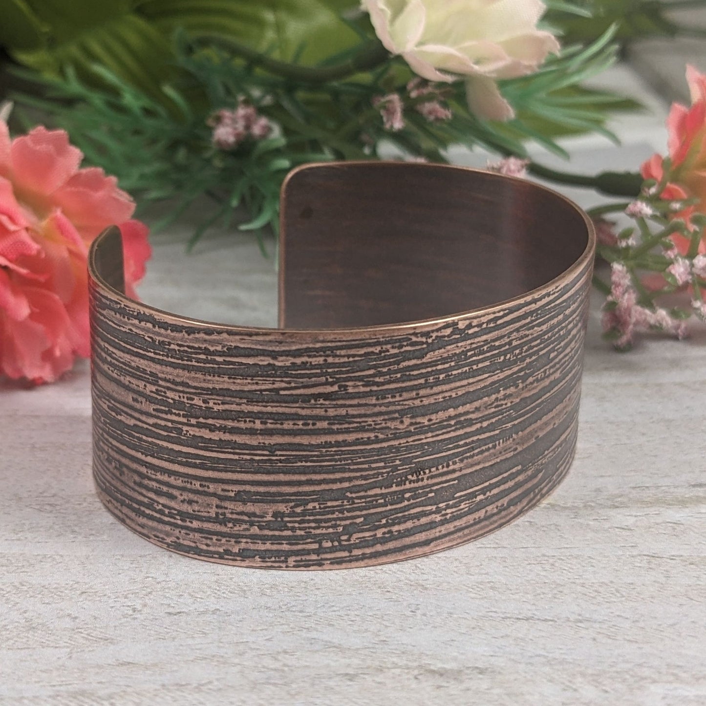 One inch wide copper cuff bracelet with an impressed texture that resembles raw silk fabric. The texture is horizontal and covers the entire cuff.