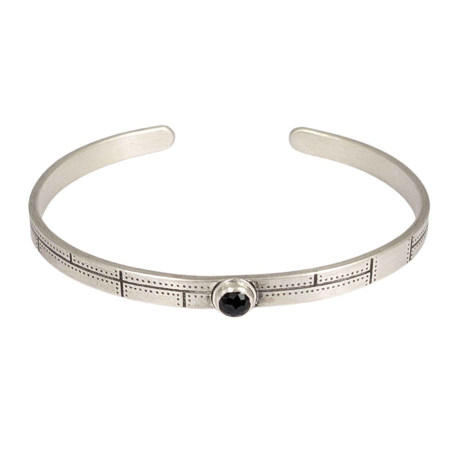Narrow sterling silver cuff bracelet. The bracelet has a riveted panel design and features a rose cut black spinel gemstone.