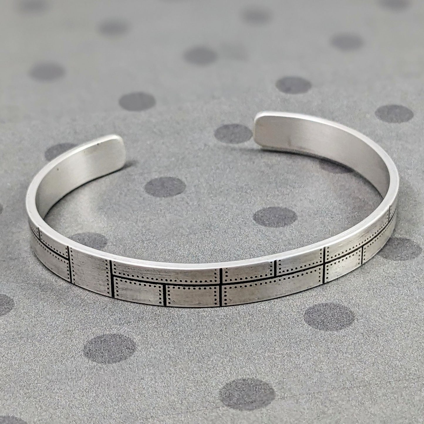 Rectangular sterling silver cuff with a riveted panel pattern. 