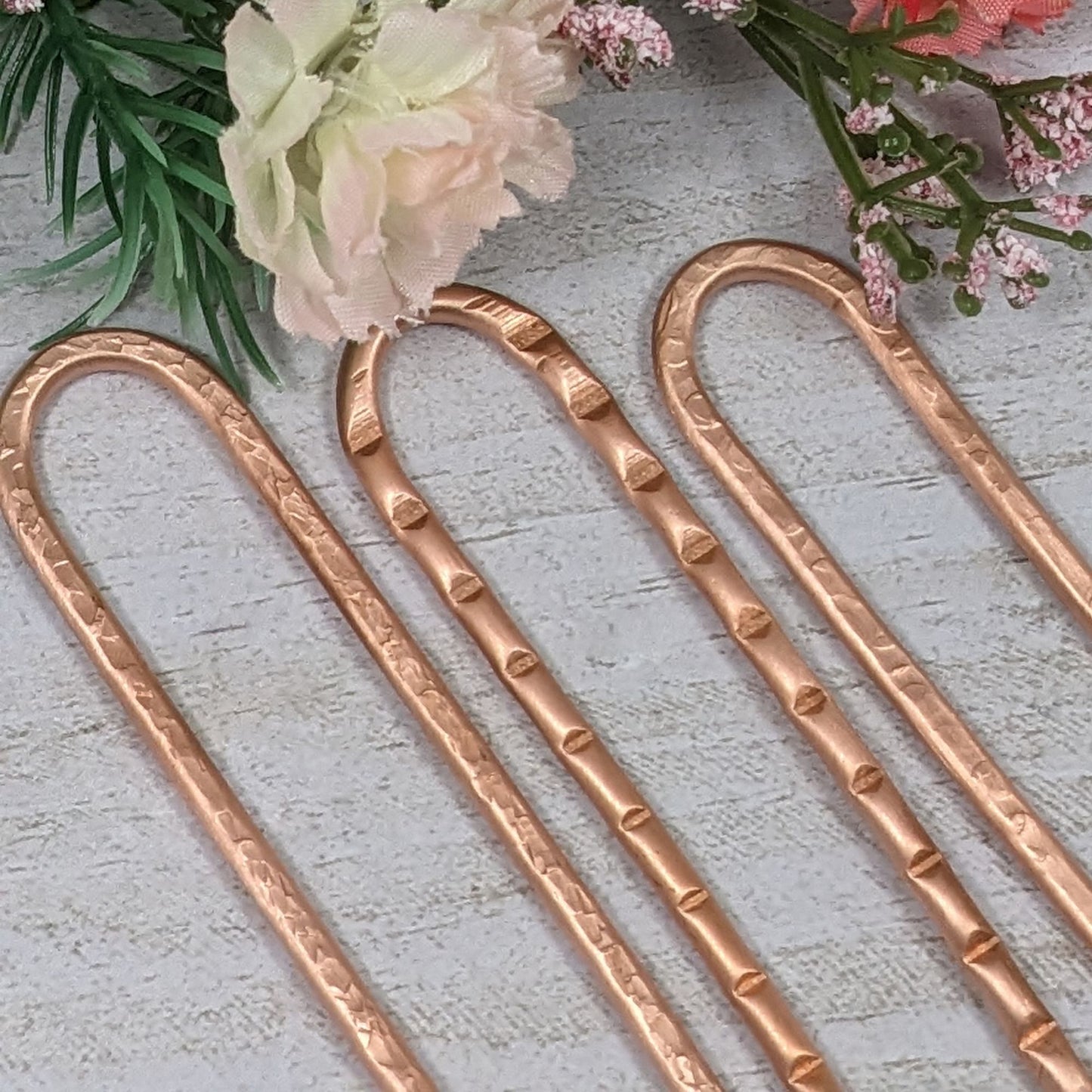 Three small copper hair forks with textured metal.