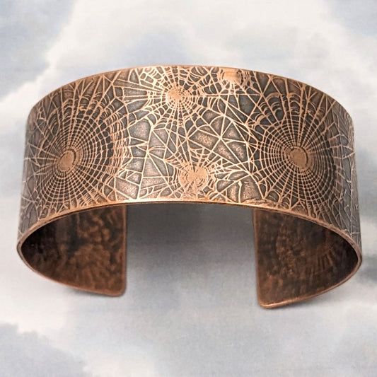 Wide copper cuff bracelet with impressed pattern of various sizes of spiderwebs