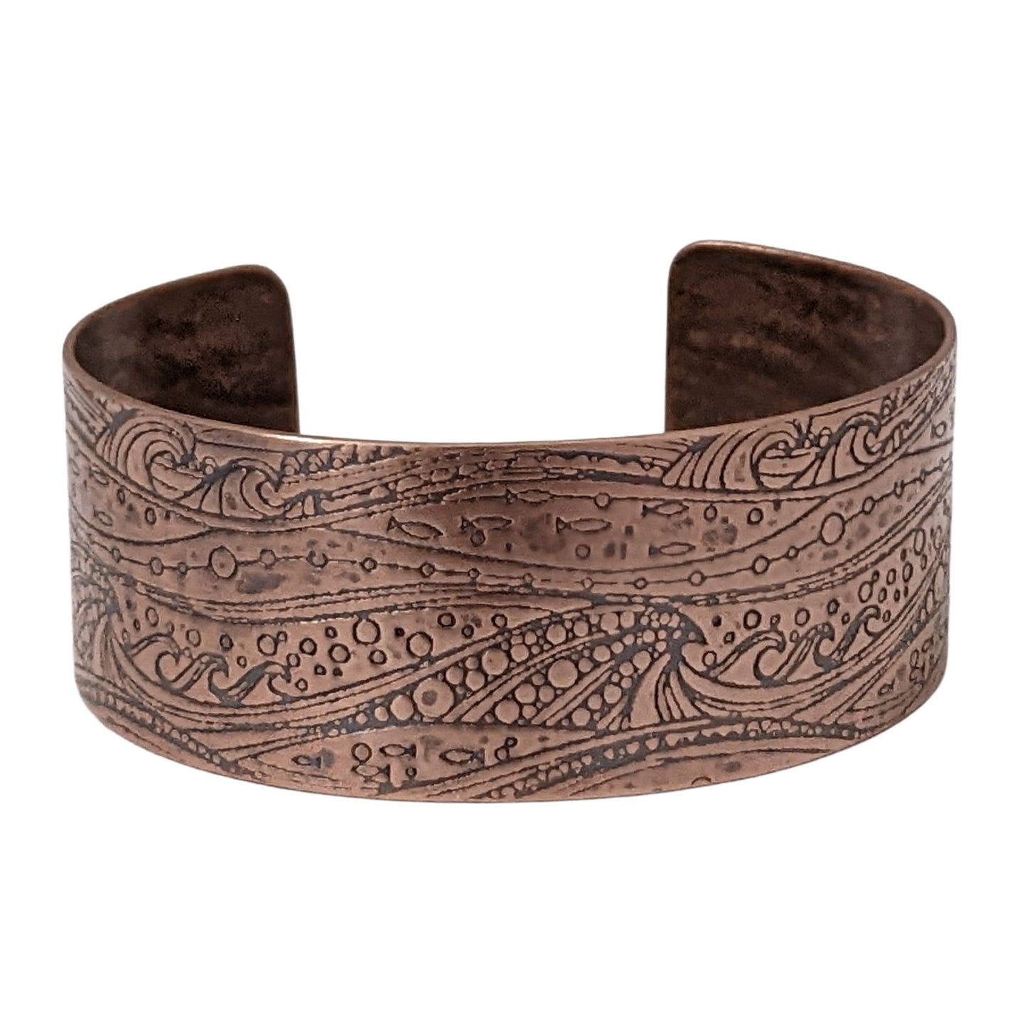 One inch wide copper cuff with a pattern of cresting waves, small fish, and air bubbles. The impression is darkened to highlight the details