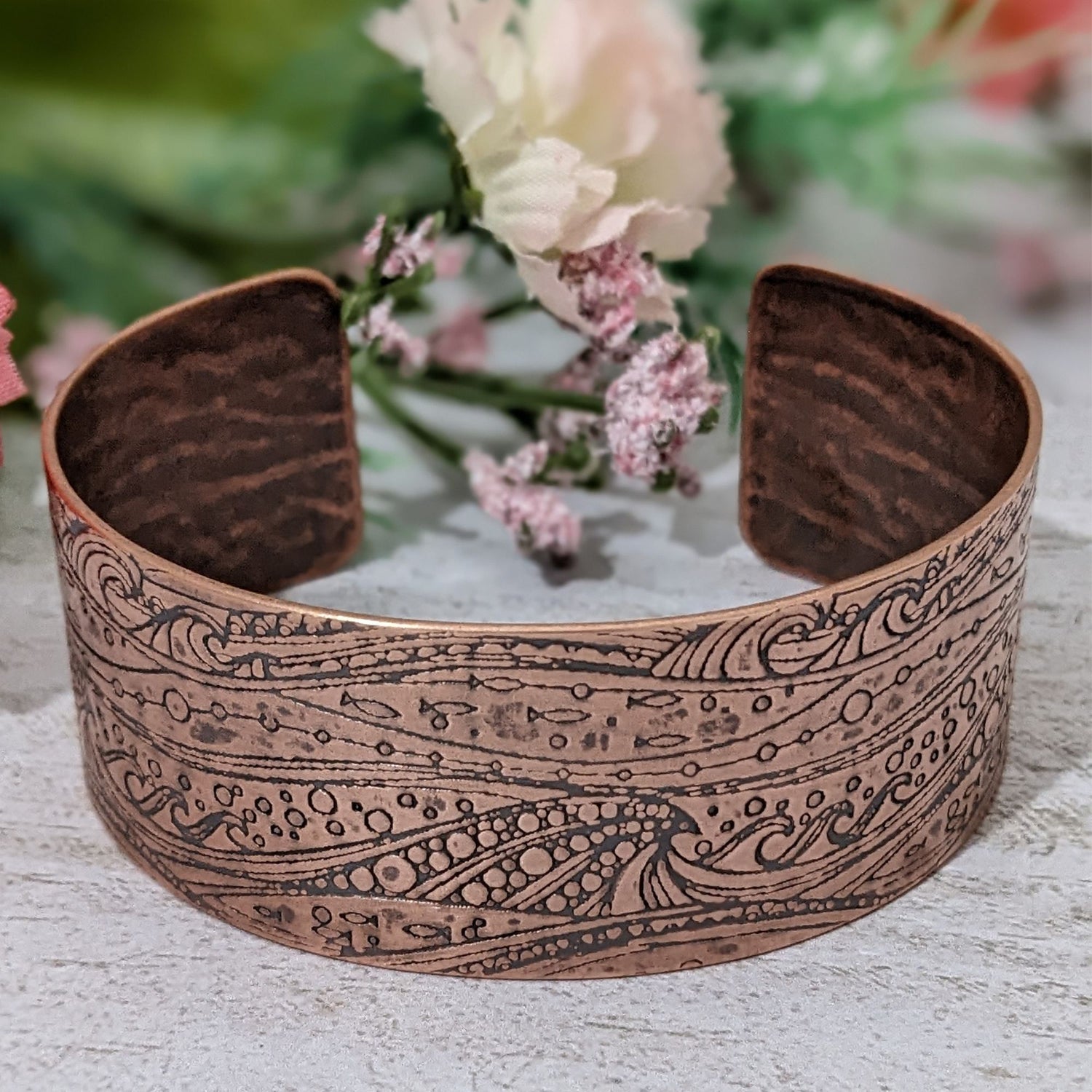 One inch wide copper cuff with a pattern of cresting waves, small fish, and air bubbles. The impression is darkened to highlight the details