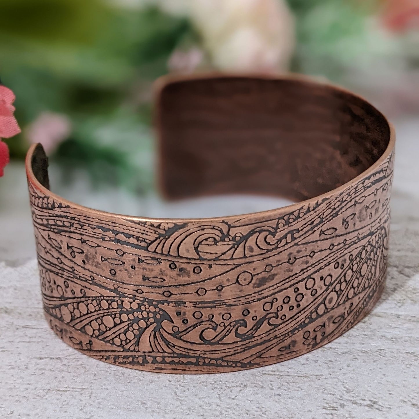 One inch wide copper cuff with a pattern of cresting waves, small fish, and air bubbles. The impression is darkened to highlight the details