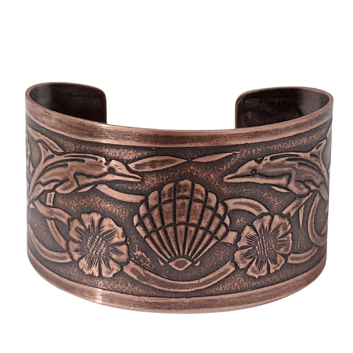 Wide tapered copper cuff bracelet with sea life design. Center is a seashell, with flowers and dolphins on either side.  Toward the ends of the cuff there are turtles, and a seaweed pattern is woven throughout the design.