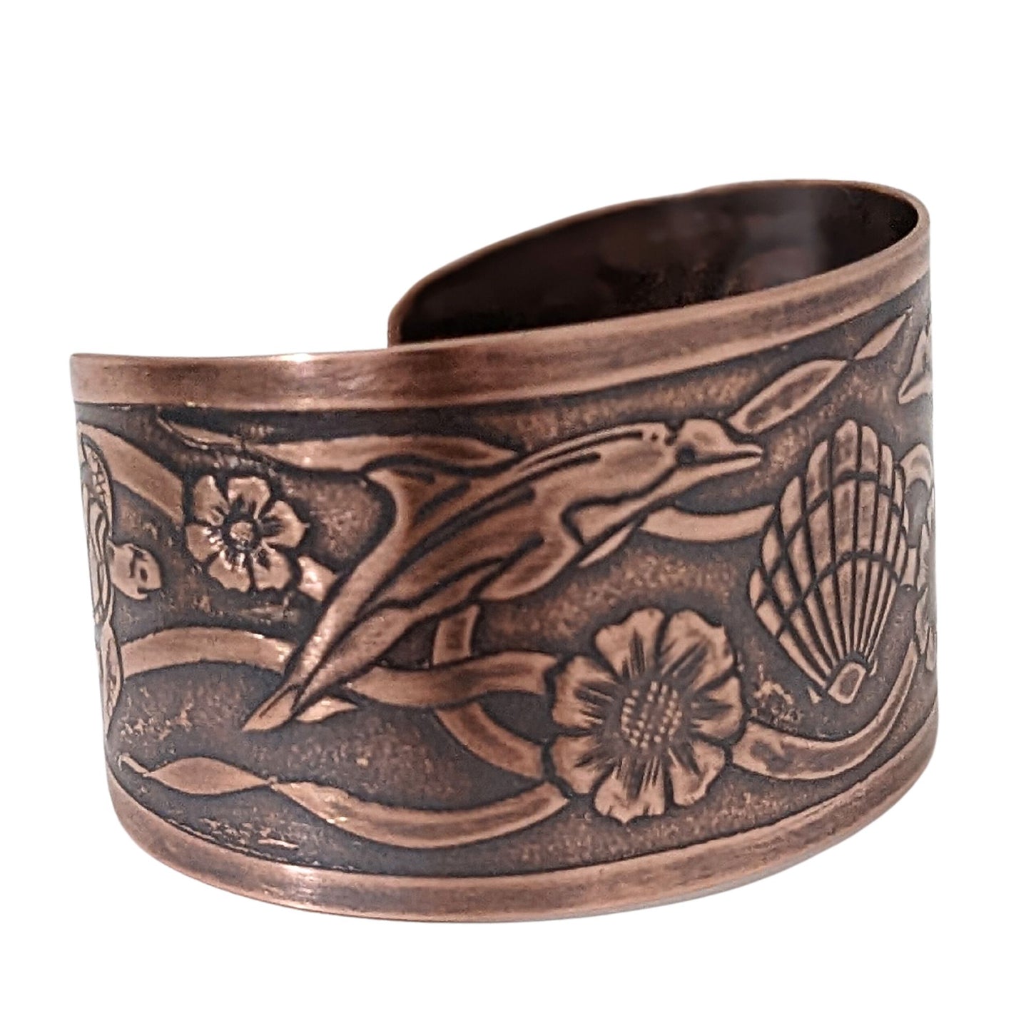 Wide tapered copper cuff bracelet with sea life design. Center is a seashell, with flowers and dolphins on either side.  Toward the ends of the cuff there are turtles, and a seaweed pattern is woven throughout the design.