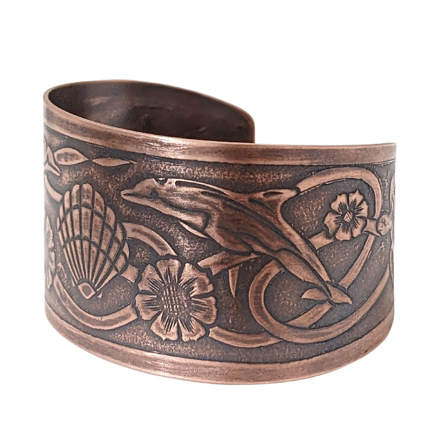 Wide tapered copper cuff bracelet with sea life design. Center is a seashell, with flowers and dolphins on either side.  Toward the ends of the cuff there are turtles, and a seaweed pattern is woven throughout the design.