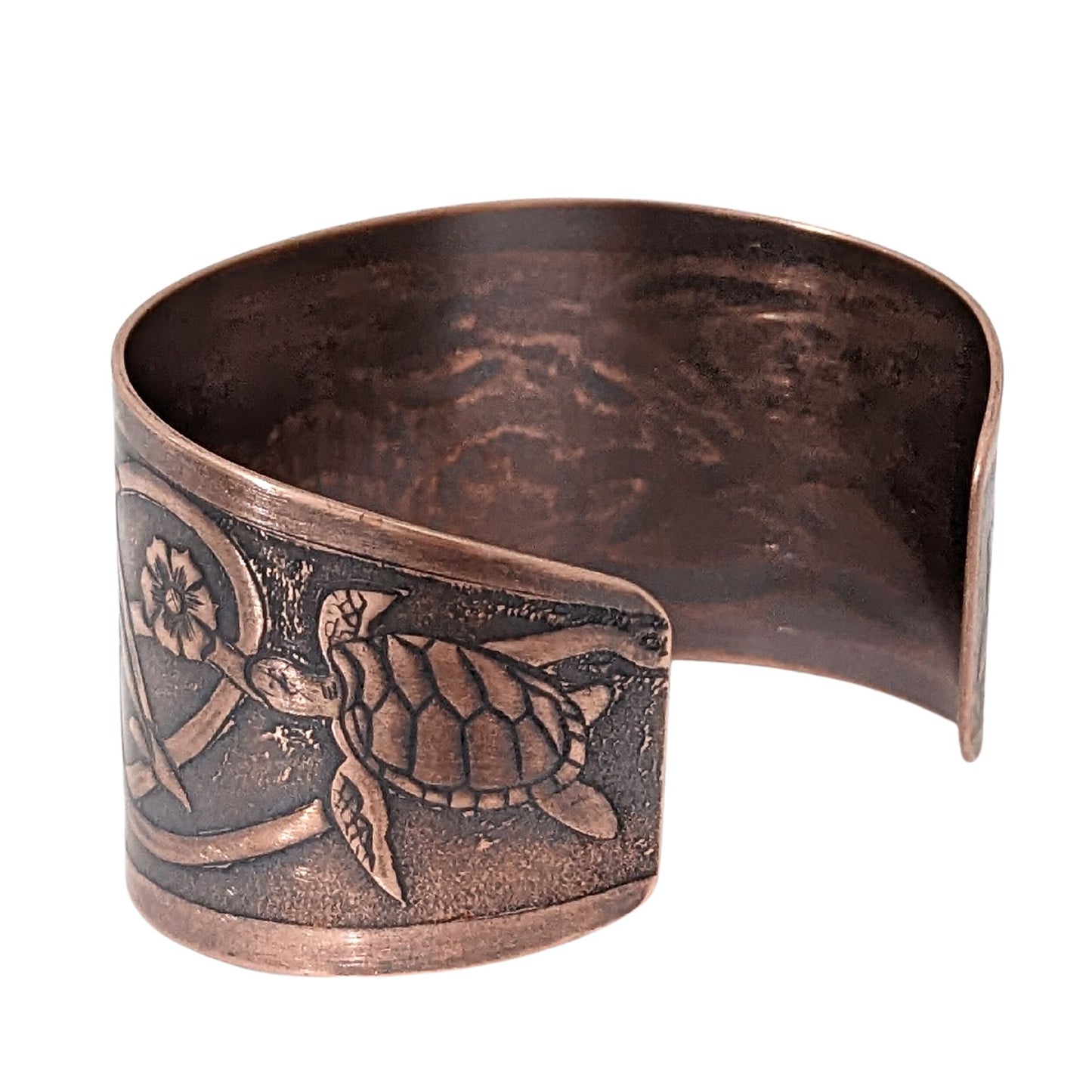 Wide tapered copper cuff bracelet with sea life design. Center is a seashell, with flowers and dolphins on either side.  Toward the ends of the cuff there are turtles, and a seaweed pattern is woven throughout the design.