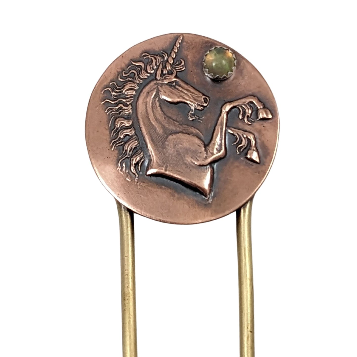 Brass hair fork with a copper design at the top. The copper is round with a raised impression of a unicorn. You can see the beard, detailed hair in the mane and on the ankles. The horn is spiraled. Above the nose there is a round gemstone meant to represent the moon.