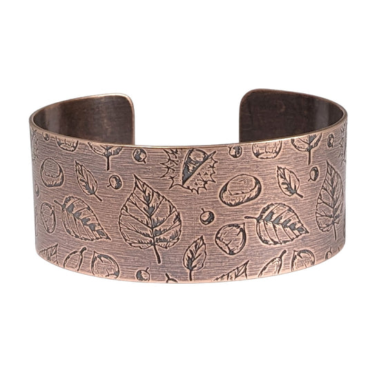 A copper cuff bracelet covered in a pattern of fall leaves and nuts