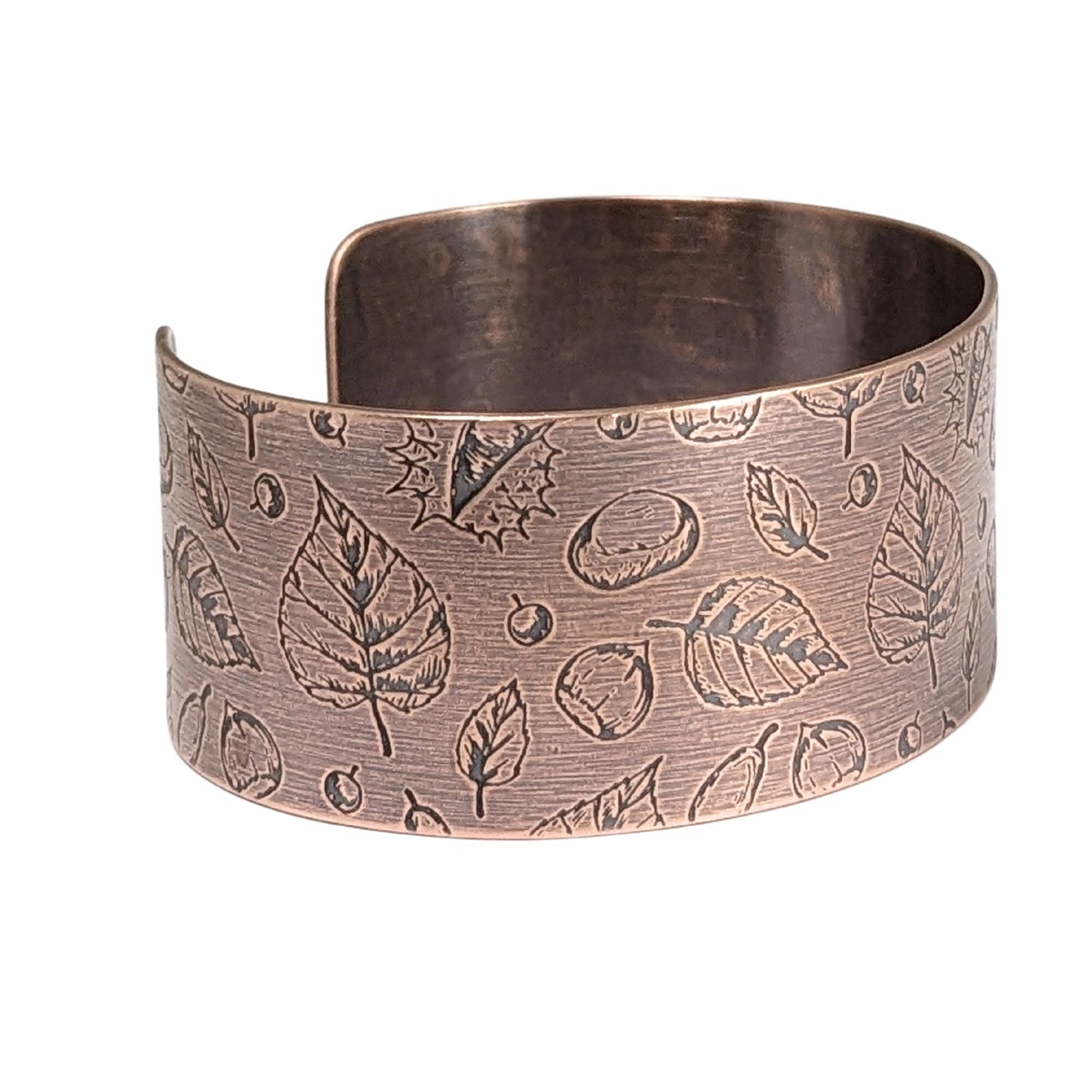 A copper cuff bracelet covered in a pattern of fall leaves and nuts