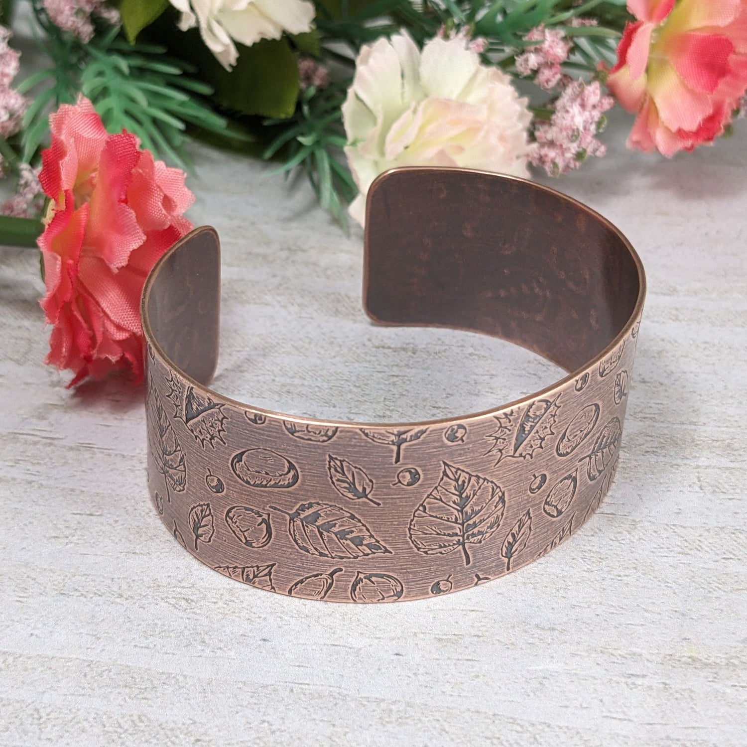 A copper cuff bracelet covered in a pattern of fall leaves and nuts