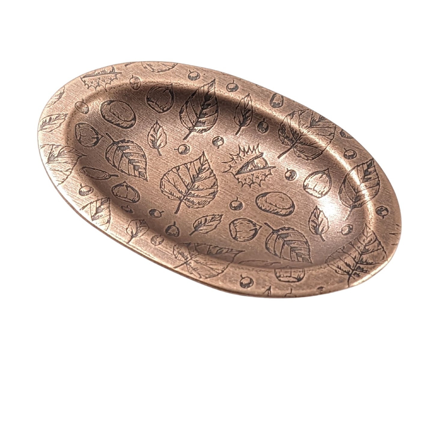 Oval copper ring dish with a raised edge. Pattern on dish is leaves, acorns, and other fall tree nuts.