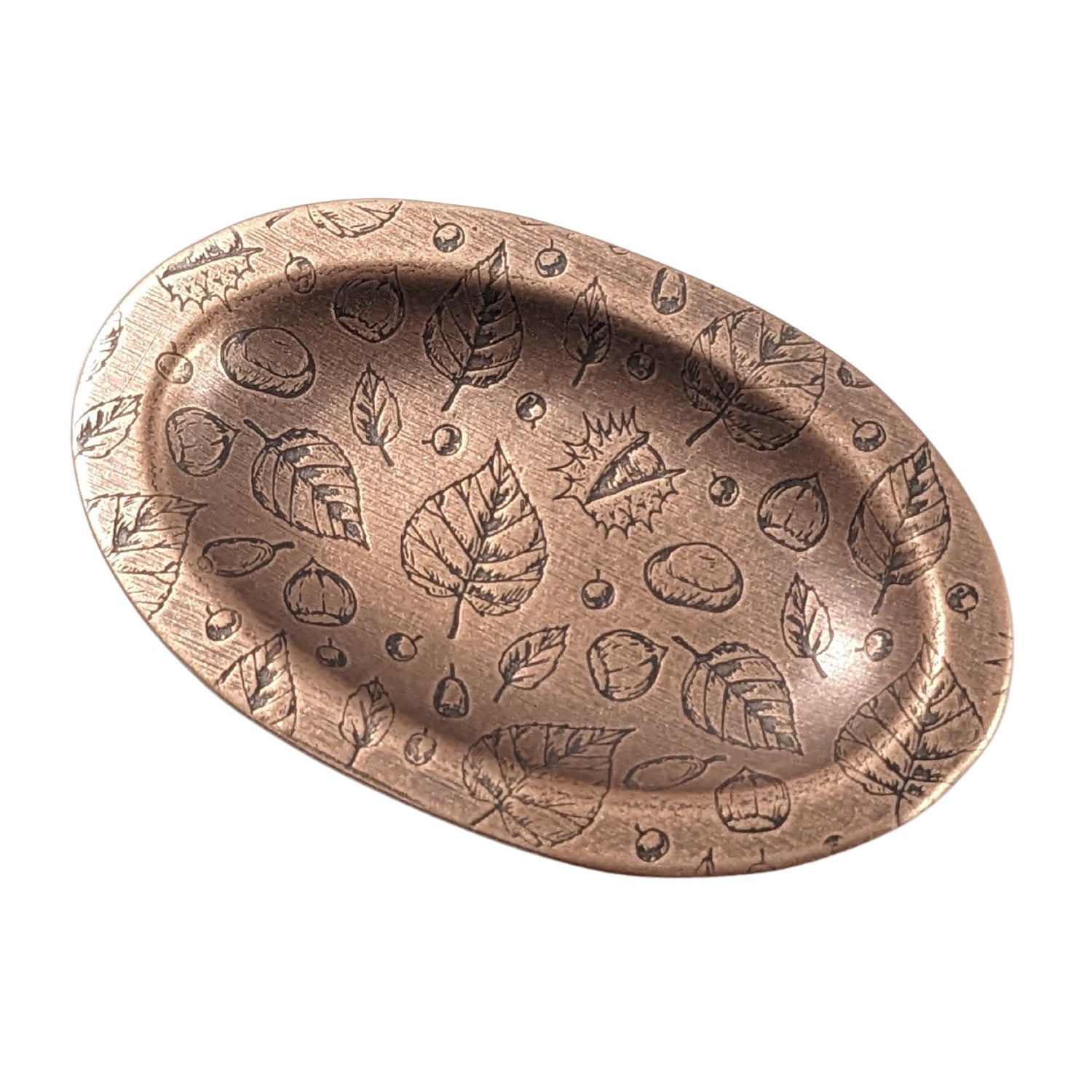 Oval copper ring dish with a raised edge. Pattern on dish is leaves, acorns, and other fall tree nuts.