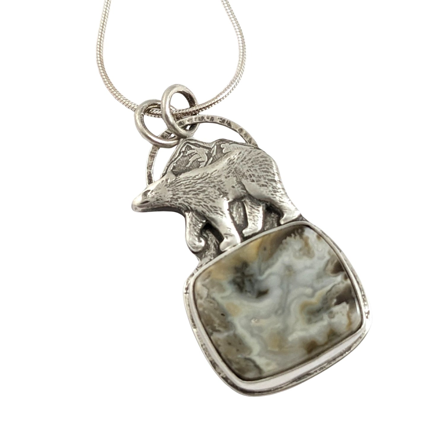 Sterling silver pendant. The top half is a bear walking against a background of mountains, the bottom half is a cabochon that looks like river rapids.