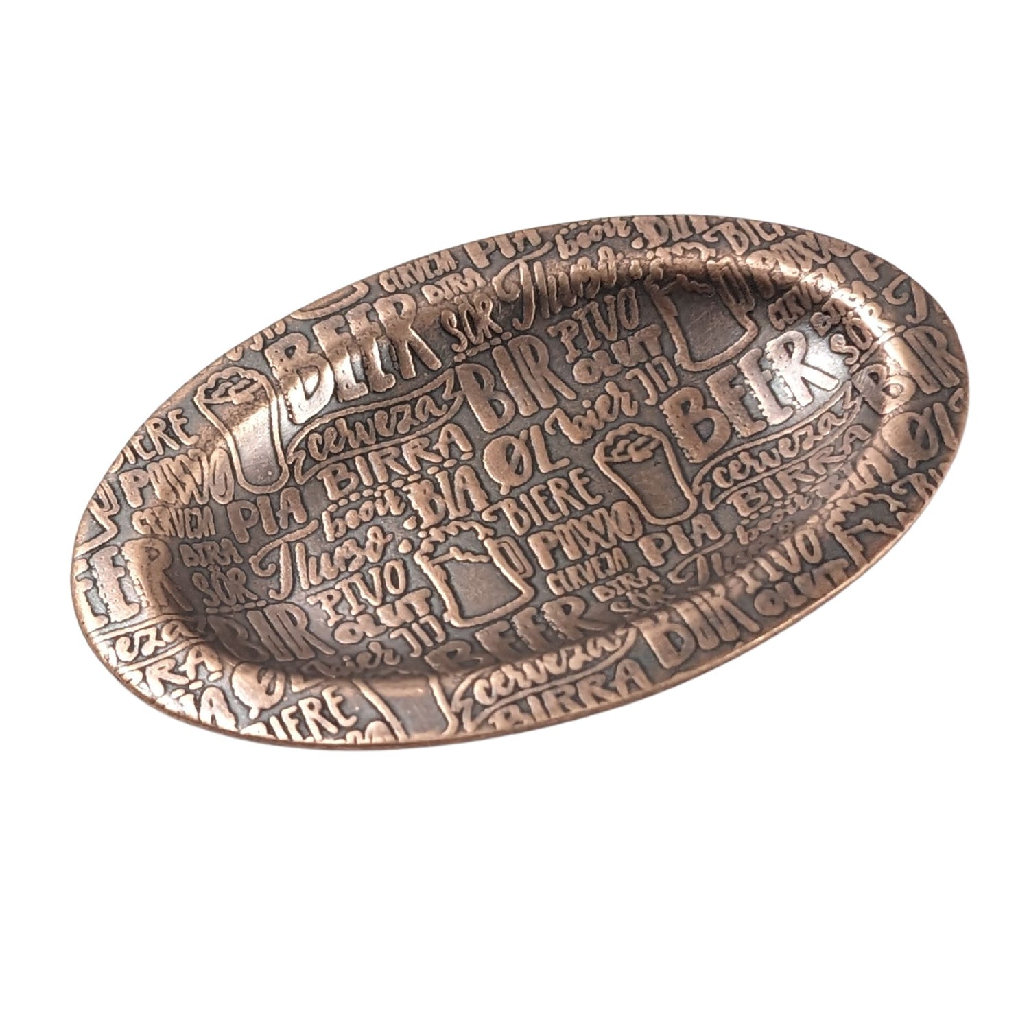 An oval copper ring dish with a raised edge. The dish has an impressed pattern made up of the word beer in many languages.