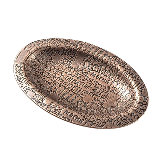 An oval copper ring dish with a raised edge. The dish has an impressed pattern of coffee order names.