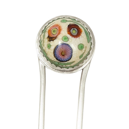 Sterling silver hair fork with a round lampwork glass stone at the top. The glass is pale yellow with ribbons of green around the edge and three abstract forms that look like flowers - one red, one orange, and one blue/pink.