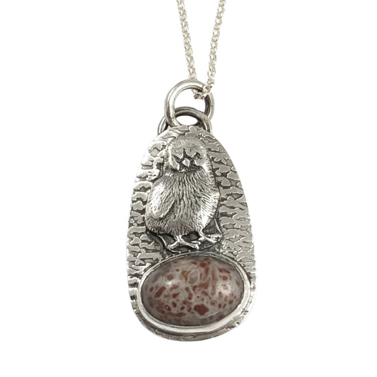 Egg shaped sterling silver pendant with a three dimensional baby chick above an oval speckled stone. The background is textured.