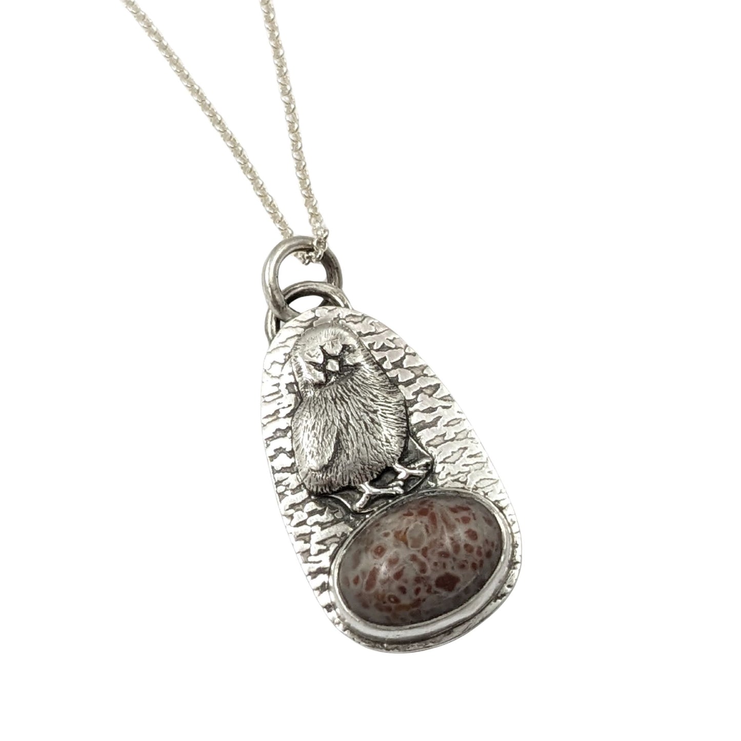 Egg shaped sterling silver pendant with a three dimensional baby chick above an oval speckled stone. The background is textured.