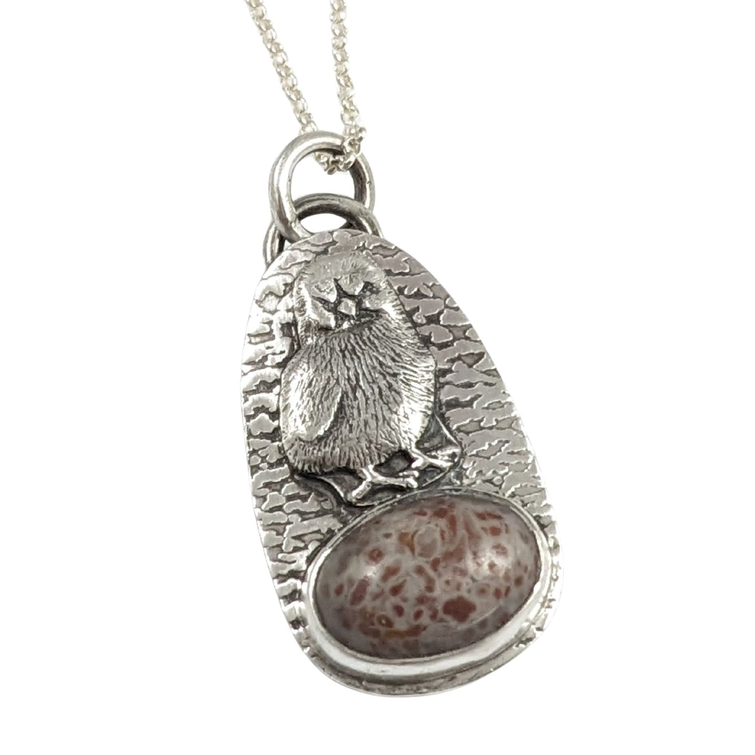 Egg shaped sterling silver pendant with a three dimensional baby chick above an oval speckled stone. The background is textured.
