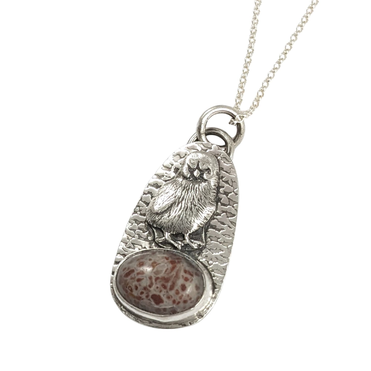 Egg shaped sterling silver pendant with a three dimensional baby chick above an oval speckled stone. The background is textured.