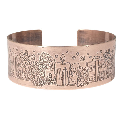 copper cuff bracelet with a christmas theme. the cuff is covered in impressions of candles, wrapped gifts, and evergreens