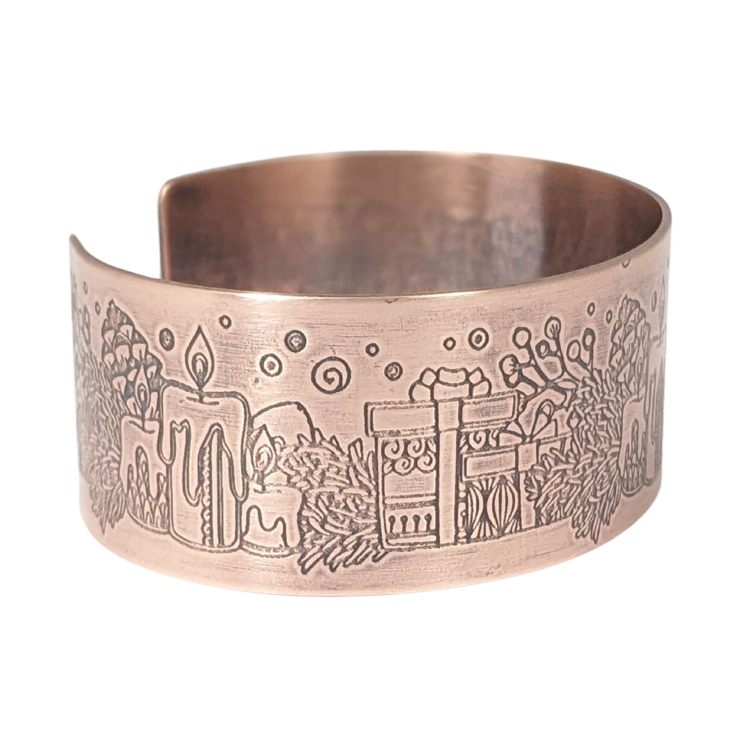 copper cuff bracelet with a christmas theme. the cuff is covered in impressions of candles, wrapped gifts, and evergreens