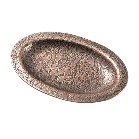 An oval copper ring dish with a raised edge. The dish has an impressed pattern of clouds.
