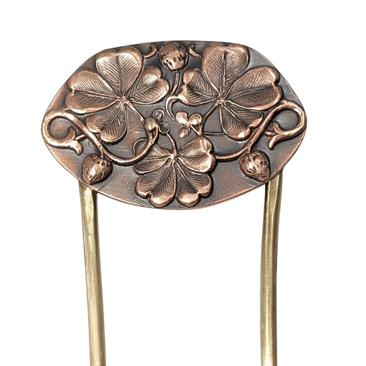 An oval copper hair fork with an emobsed design of three large four leaf clovers. Accented with vines and three small strawberries, the forks are brass.