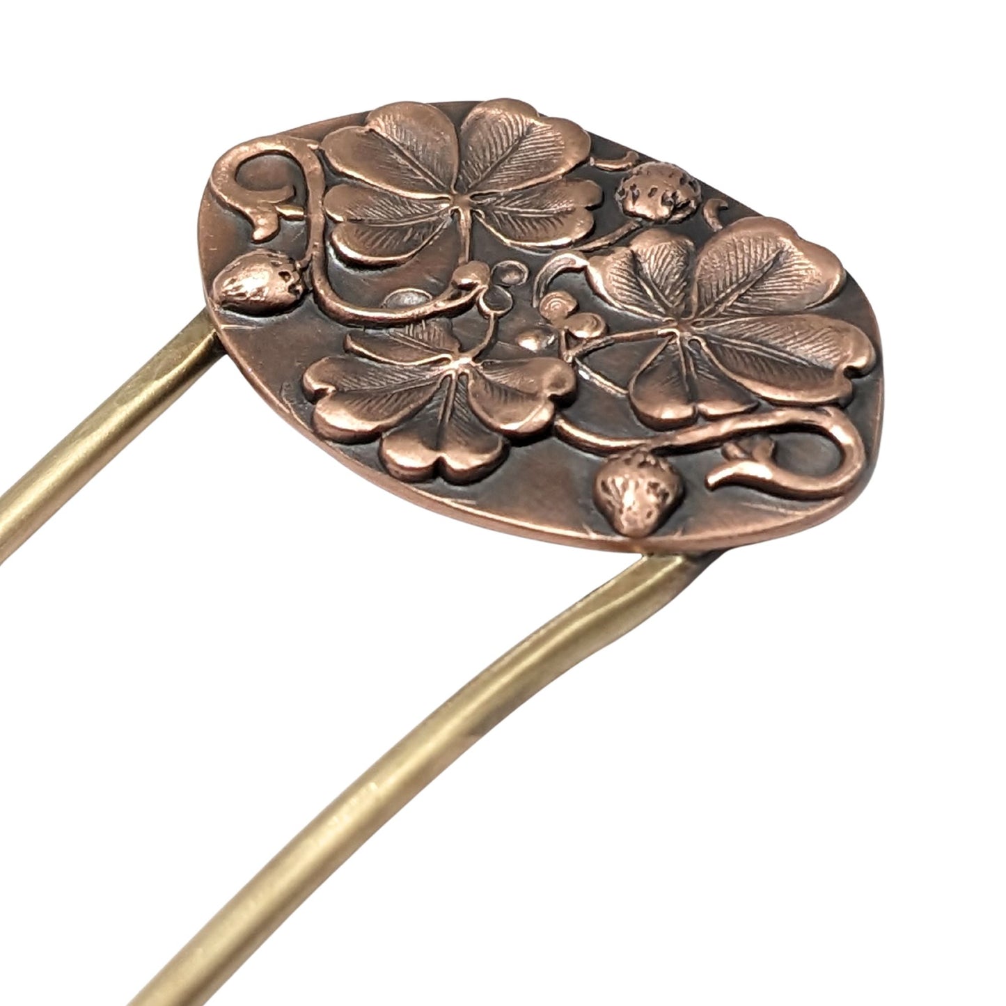 An oval copper hair fork with an emobsed design of three large four leaf clovers. Accented with vines and three small strawberries, the forks are brass.