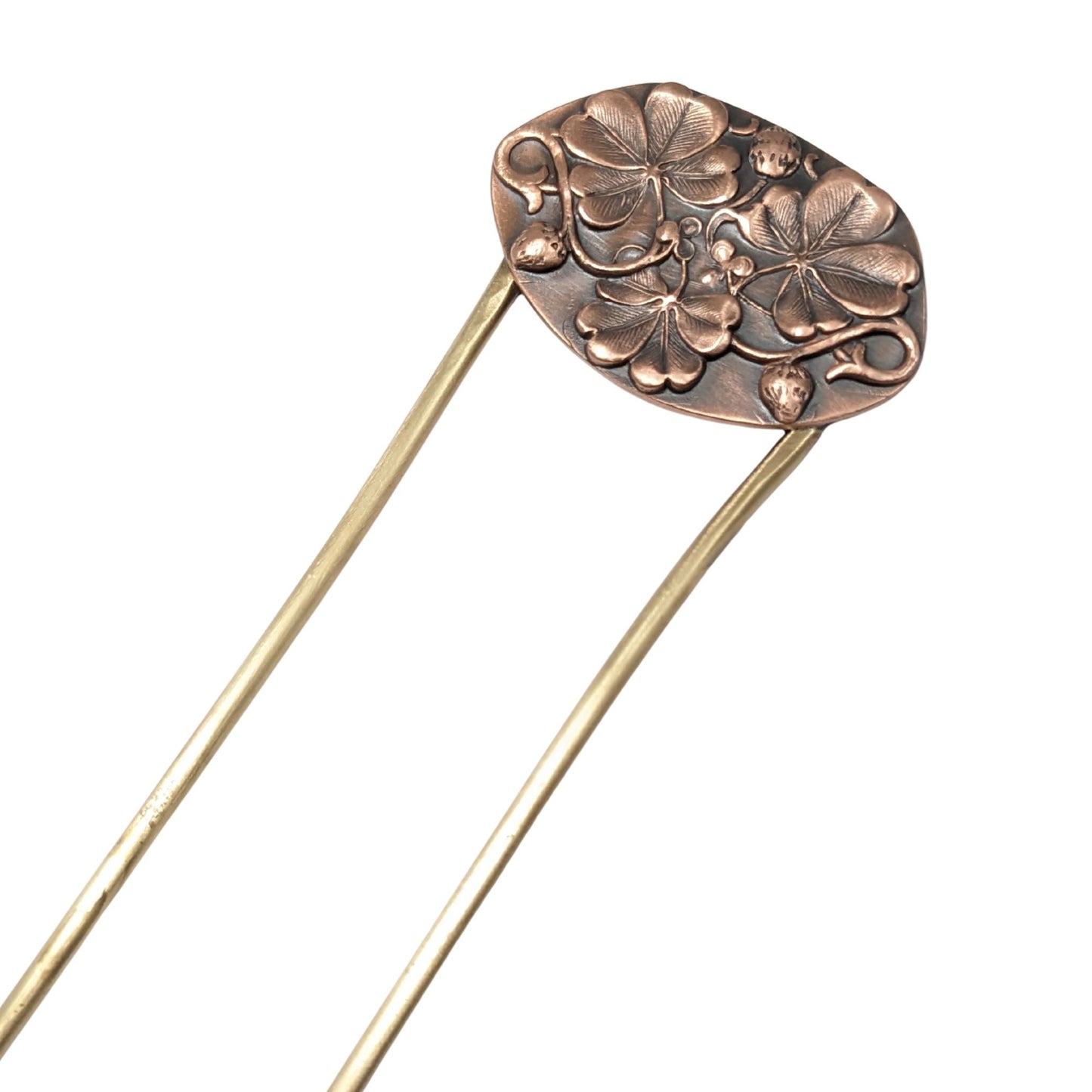 An oval copper hair fork with an emobsed design of three large four leaf clovers. Accented with vines and three small strawberries, the forks are brass.