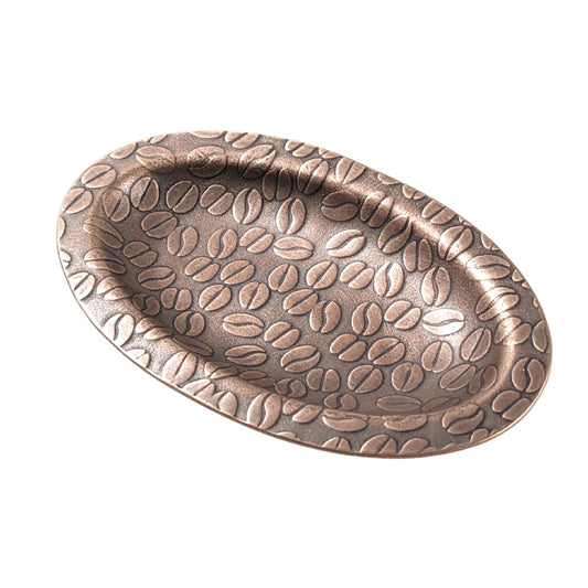 An oval copper ring dish with a raised edge. The dish has an impressed pattern of coffee beans.