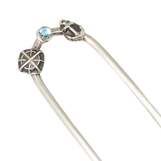 Sterling silver hair fork with three small design elements. Left is a silver compass rose, center is a rose cut blue topaz gemstone, right is a silver anchor