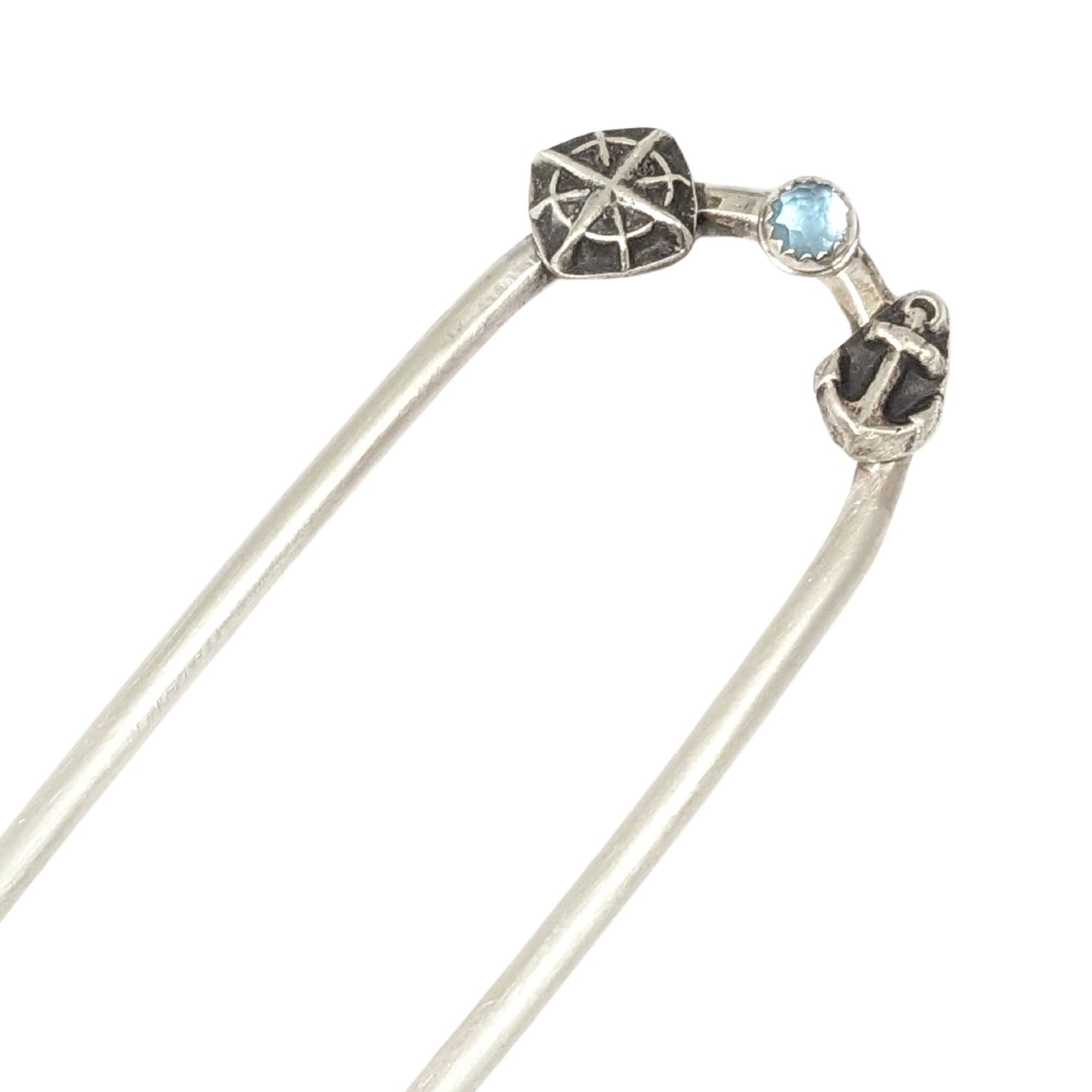 Sterling silver hair fork with three small design elements. Left is a silver compass rose, center is a rose cut blue topaz gemstone, right is a silver anchor
