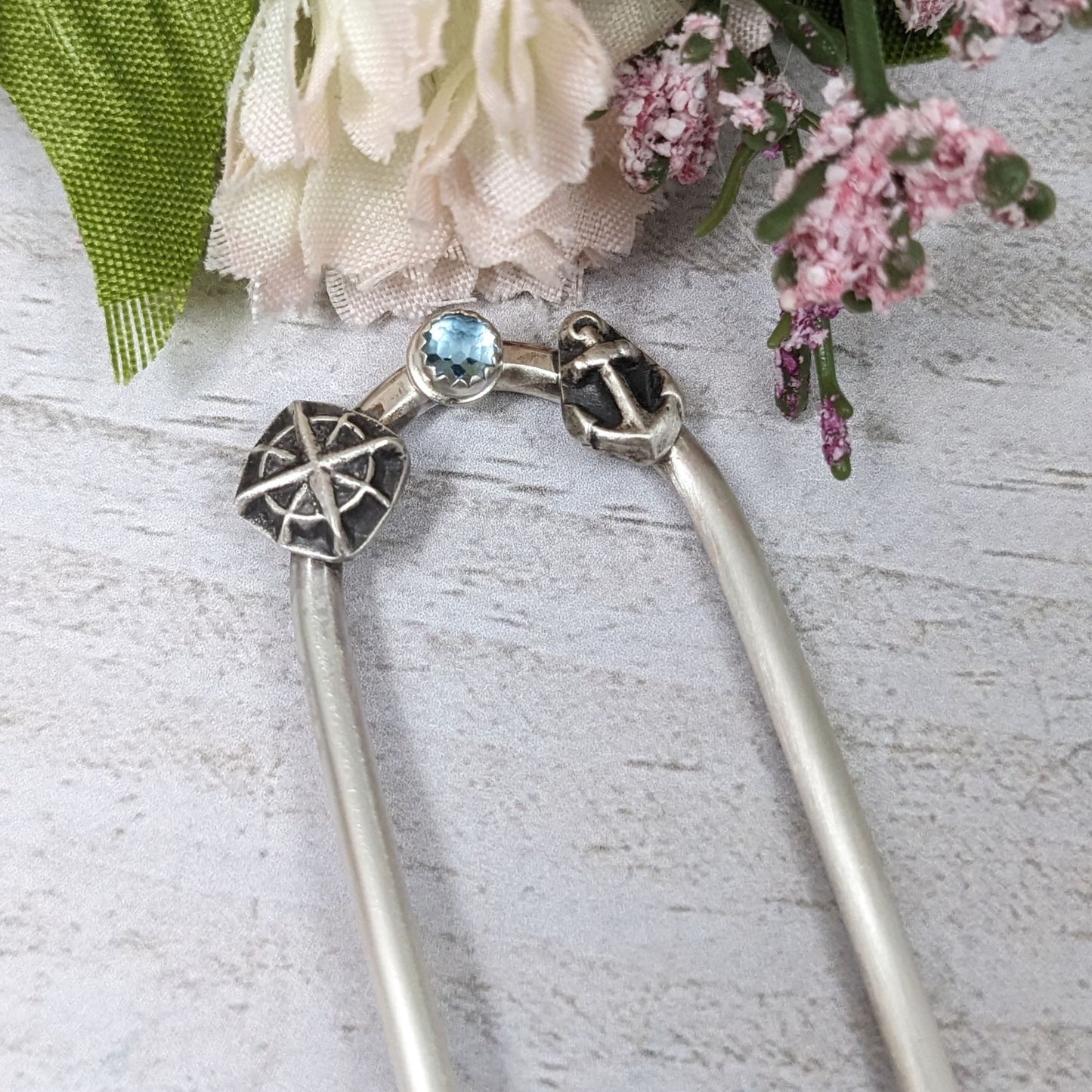 Sterling silver hair fork with three small design elements. Left is a silver compass rose, center is a rose cut blue topaz gemstone, right is a silver anchor
