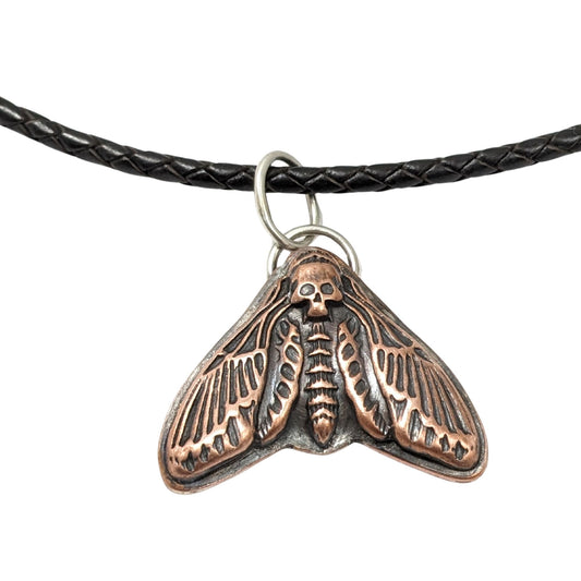Large copper moth pendant on a leather cord. The moth is called a death's head, so the head on this piece is a skull design.